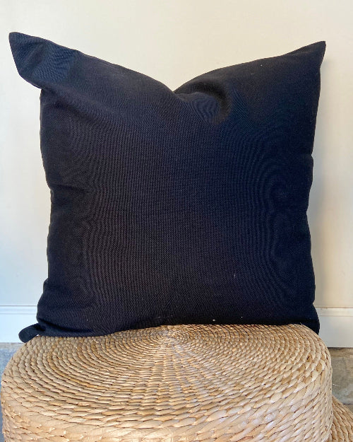 Black pillow on a woven stool against a white wall