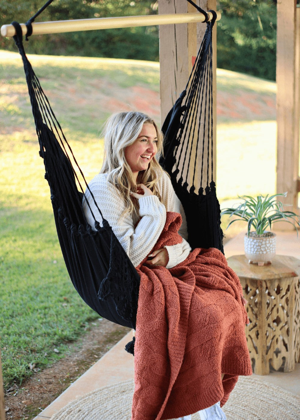 Woman relaxing in a black hammock with a red blanket outdoors.