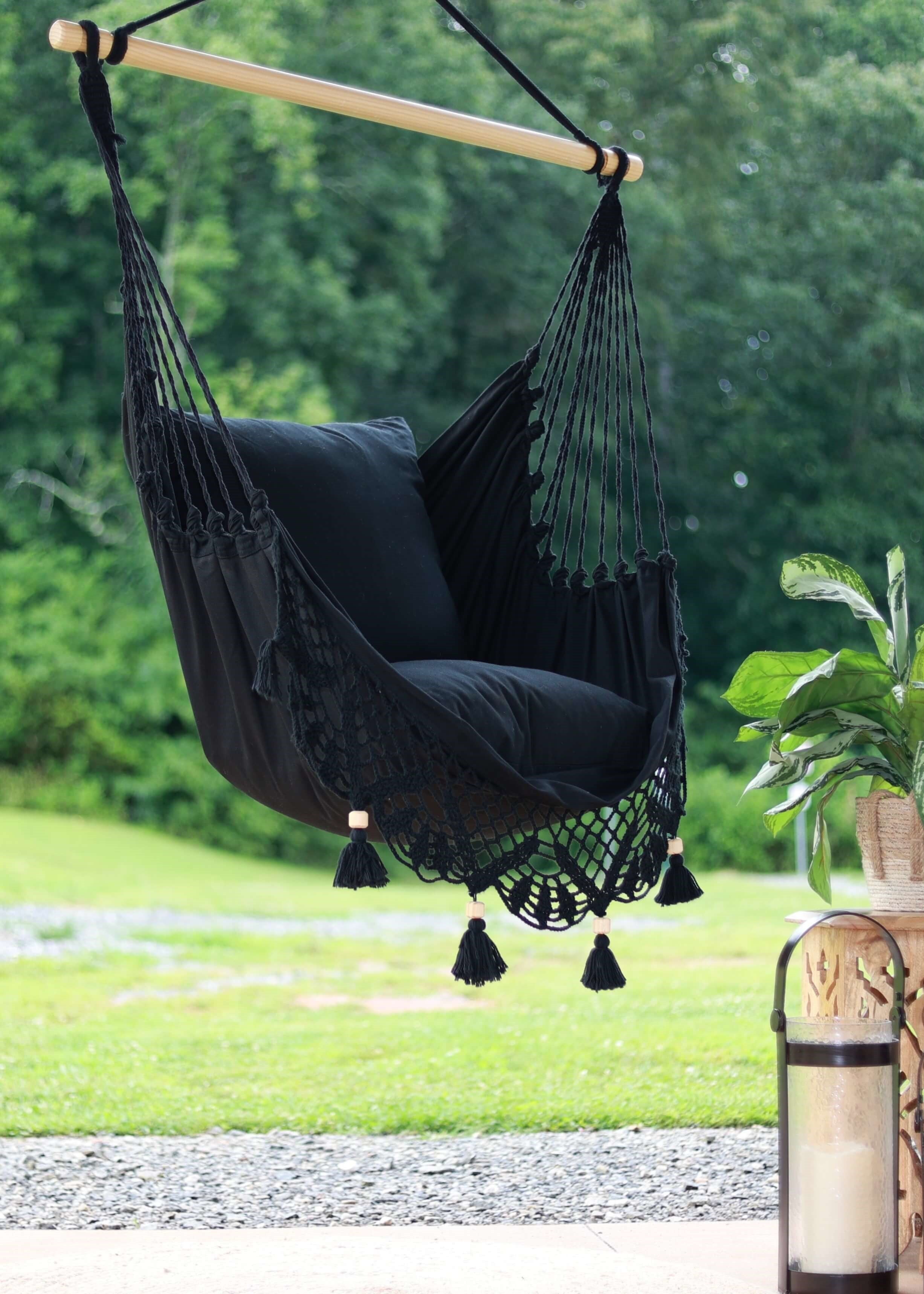 Black hammock chair with tassels hanging outdoors on a sunny day.