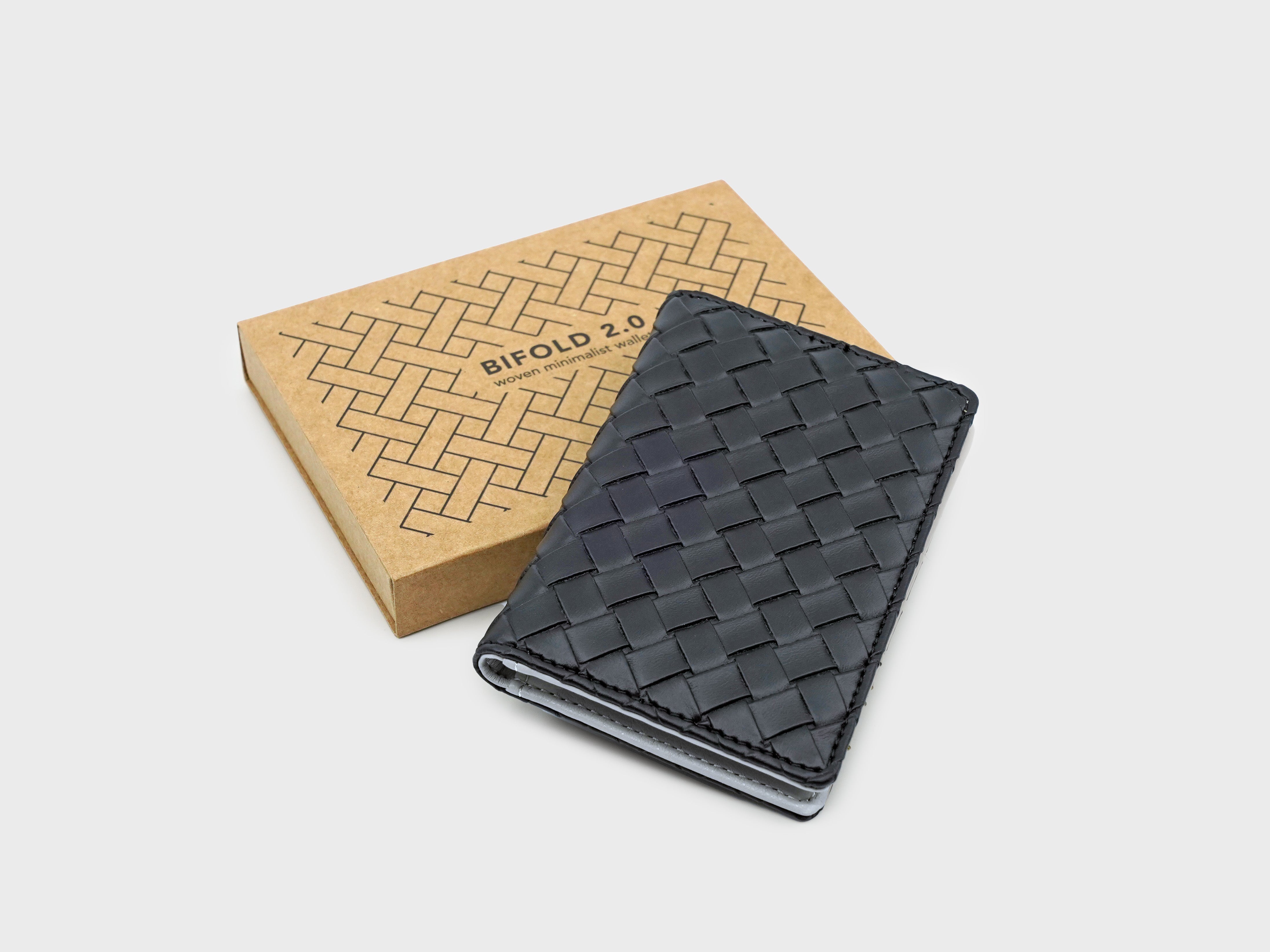 Black woven wallet next to its packaging on a light gray background