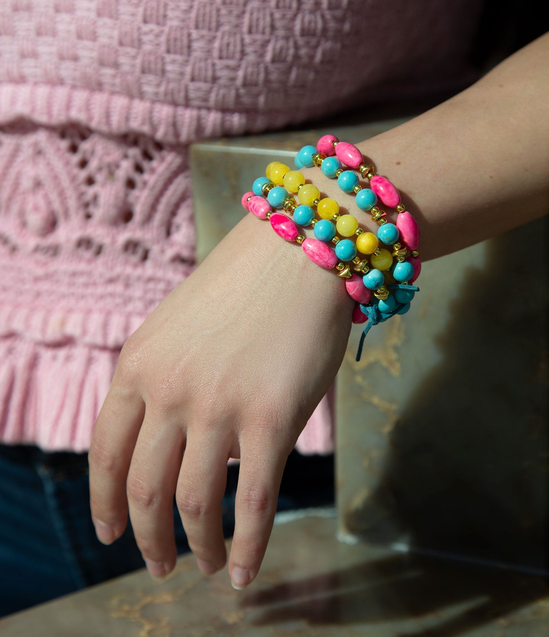 Colorful beaded bracelet on a wrist with a pink textured sweater in the background
