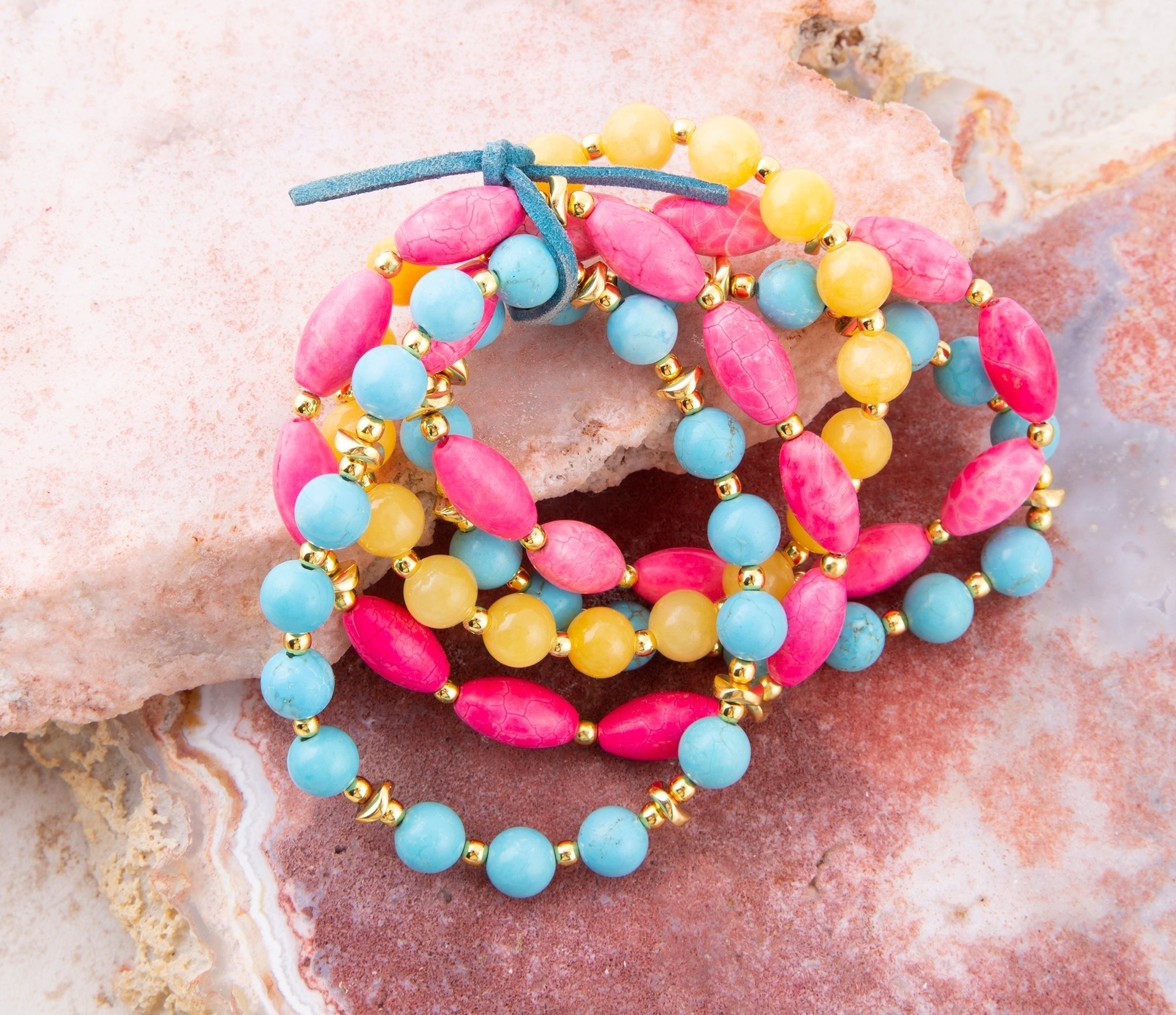 Stack of colorful beaded bracelets on a textured stone surface