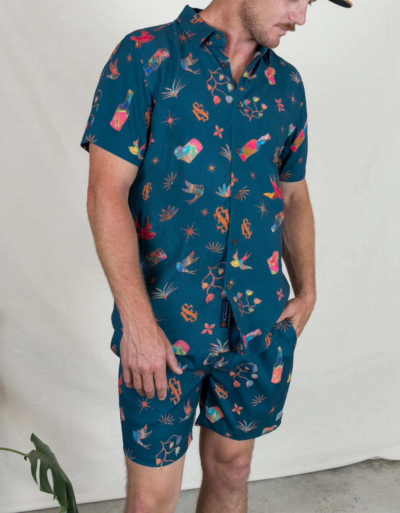 Man wearing a dark blue patterned shirt and shorts against a plain background