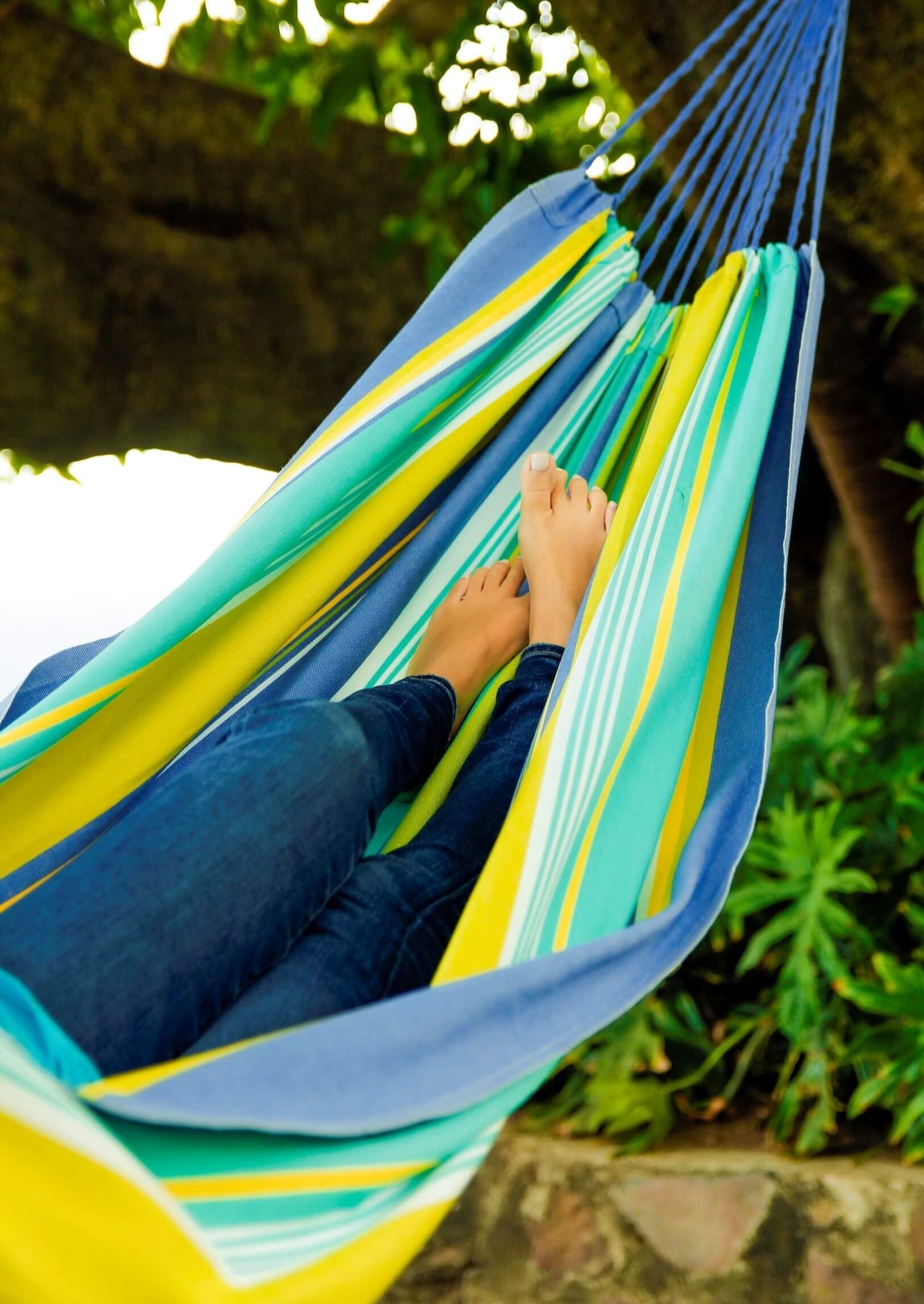 Person relaxing in a colorful striped hammock surrounded by greenery