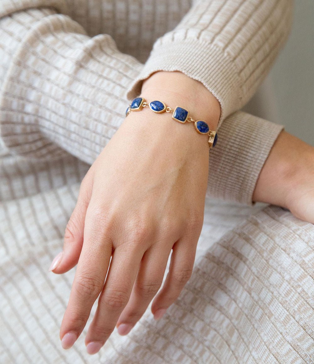 Hand wearing a gold bracelet with blue stones on a neutral background