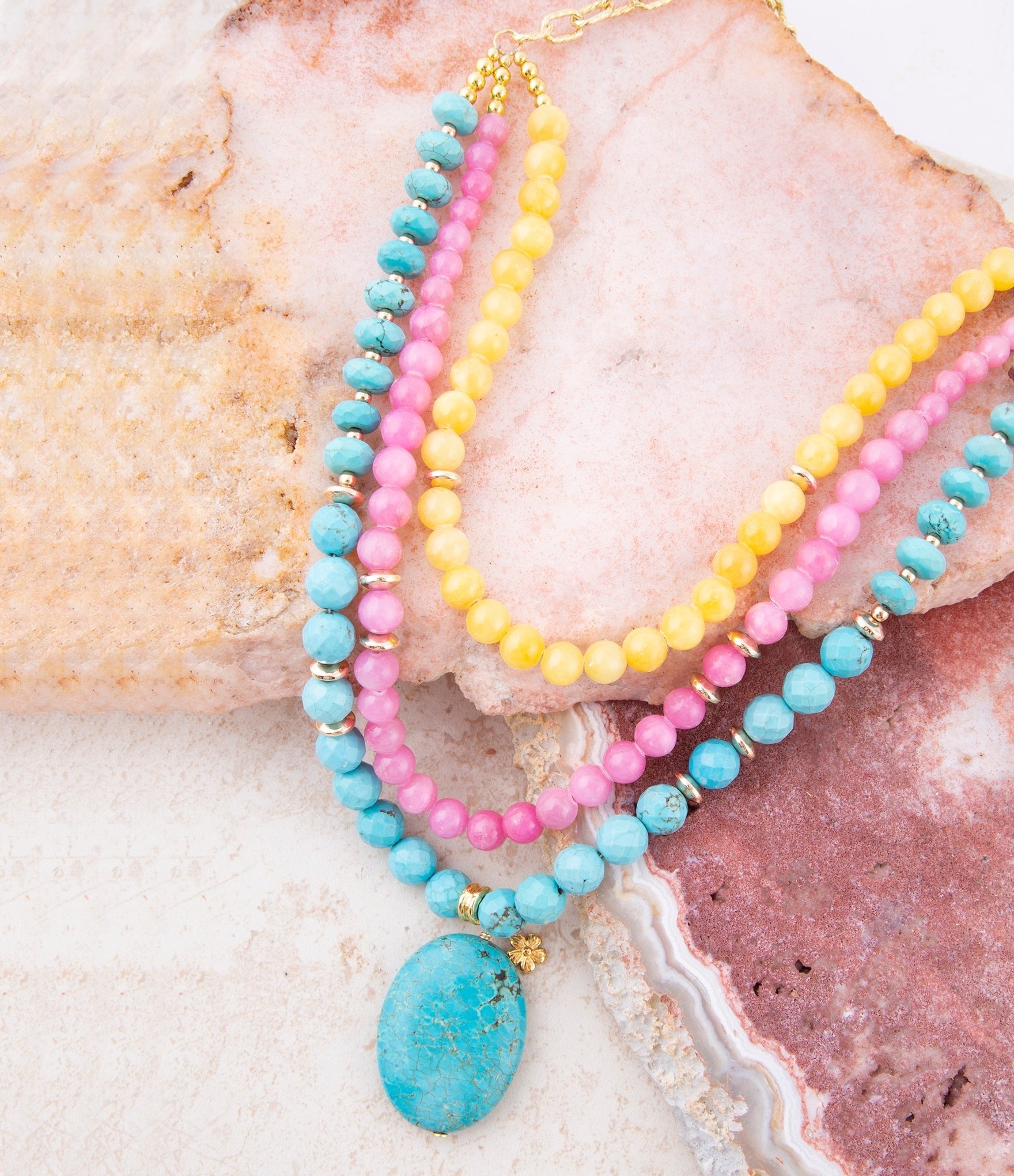 Three colorful beaded necklaces on a textured stone surface