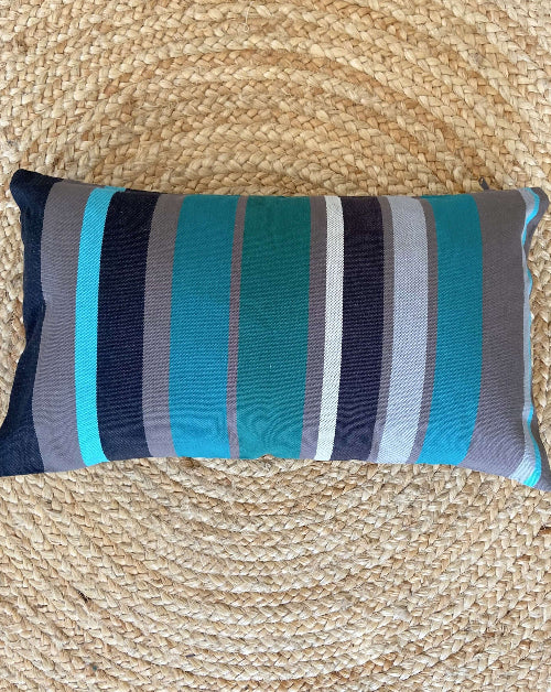 Striped pillow with blue, gray, and green colors on a woven mat background