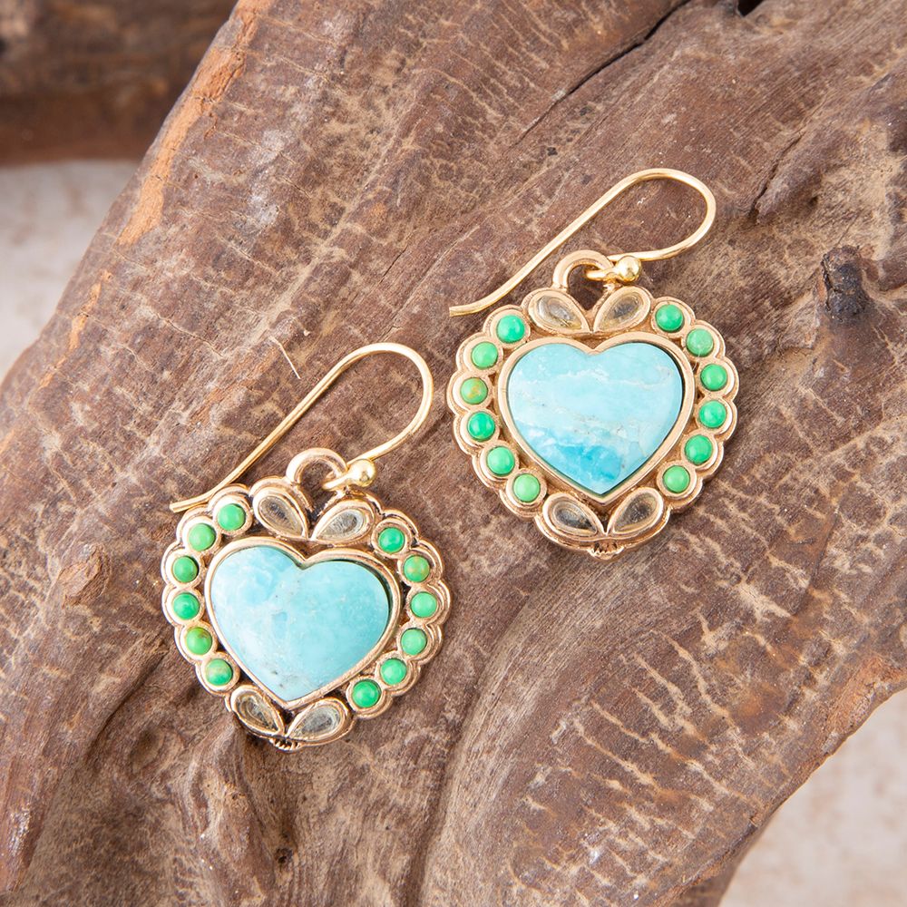 Heart-shaped earrings with turquoise centers and green accents on a wooden surface