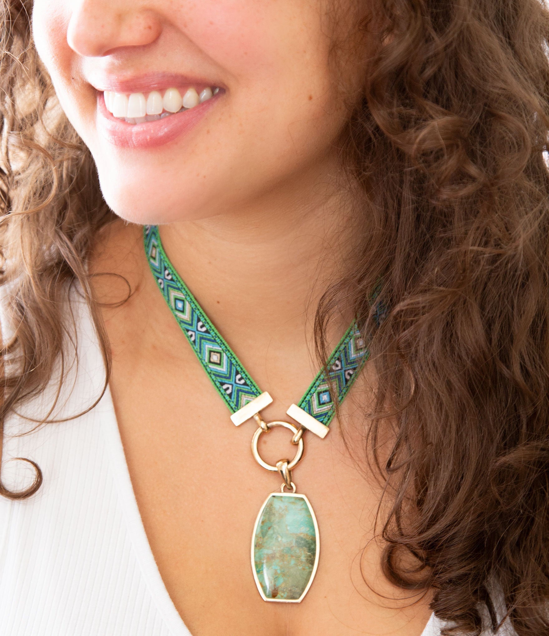 Person wearing a green necklace with a pendant, smiling.