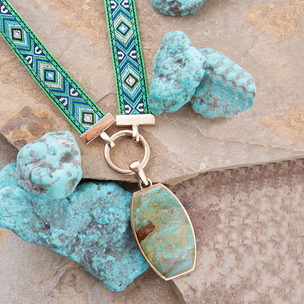 Necklace with turquoise pendant and green beaded strap on stone surface