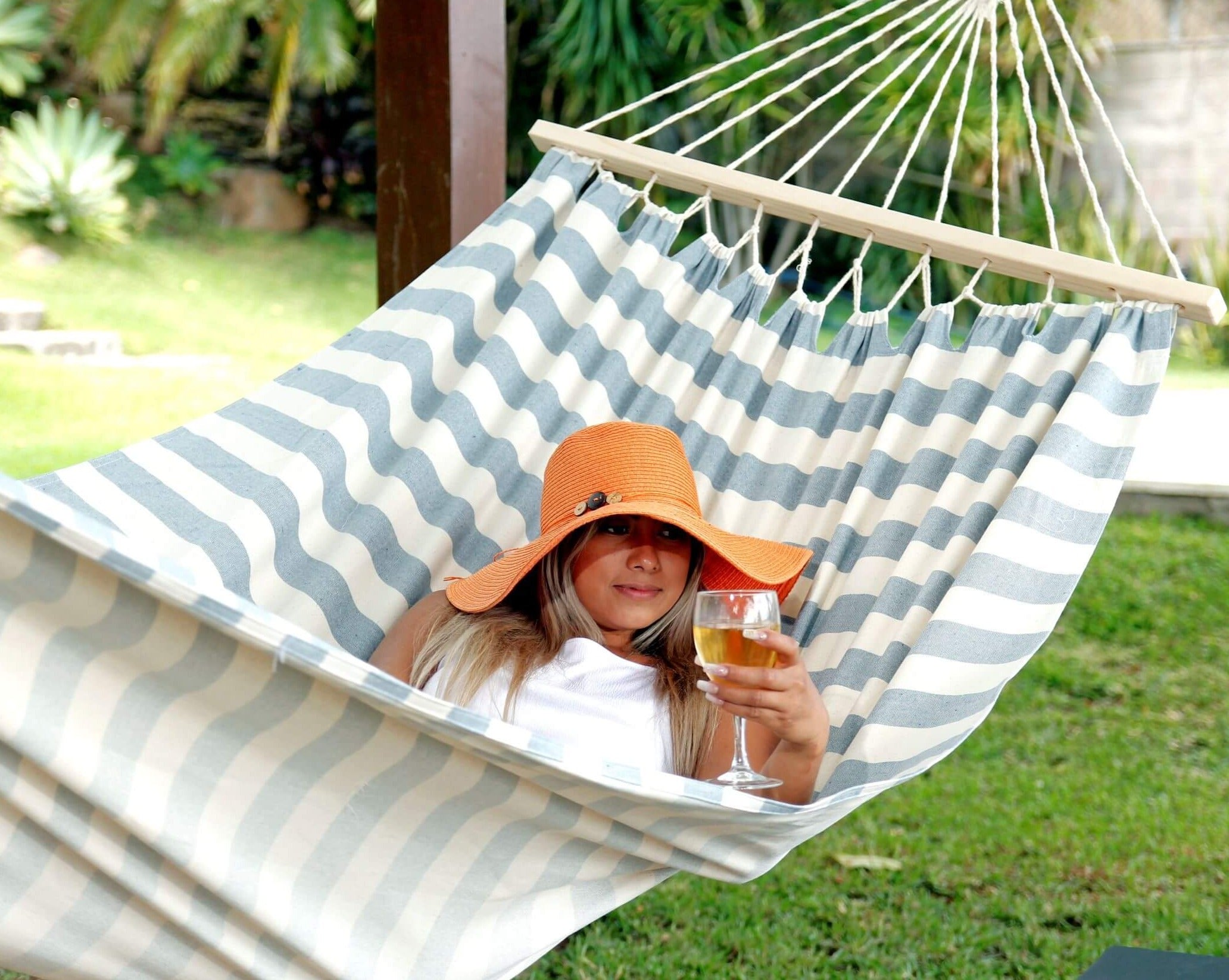 Woman relaxing in a striped hammock holding a glass of wine in a garden setting