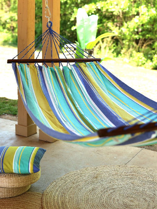 Colorful striped hammock hanging under a wooden pergola with greenery in the background.