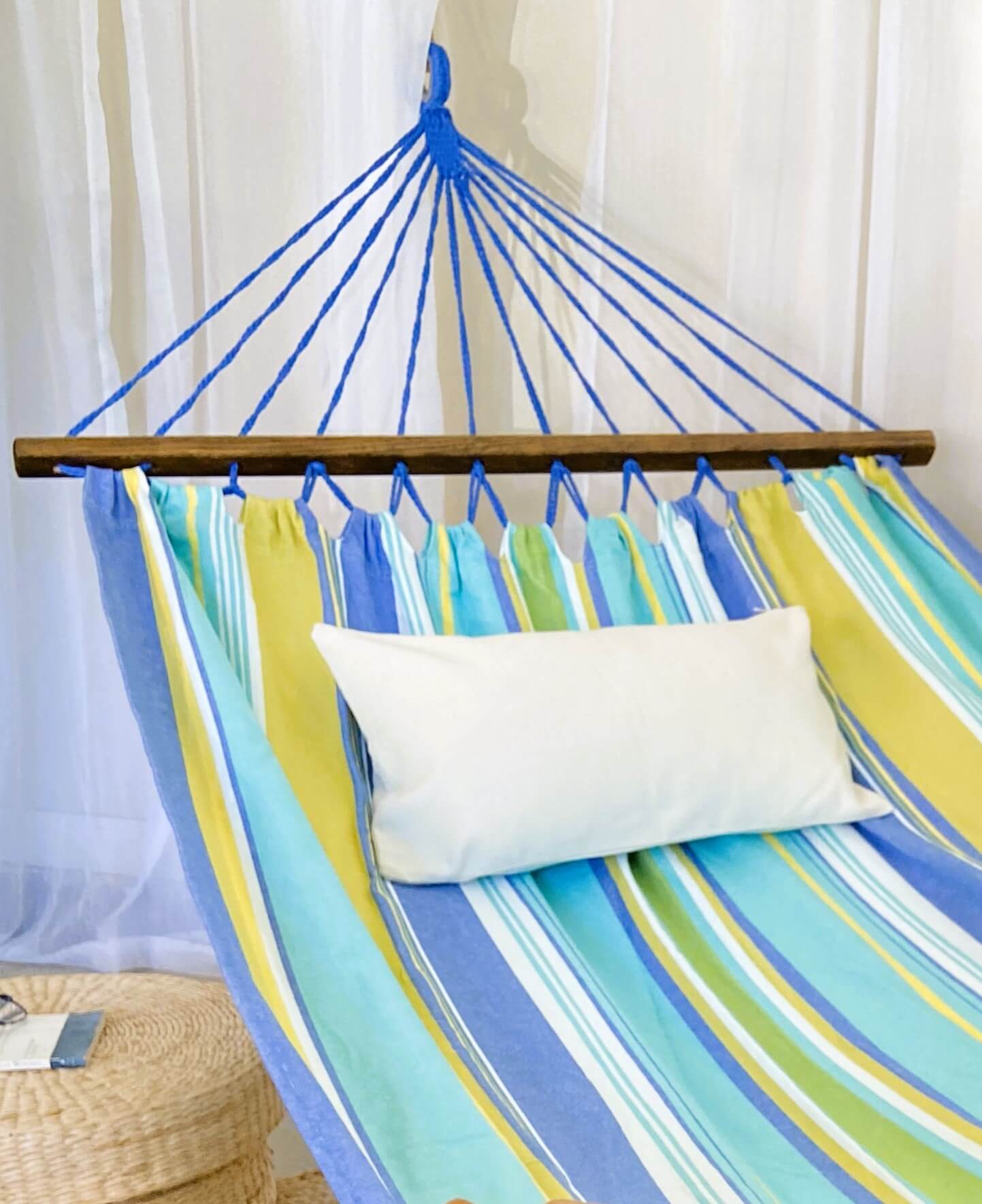 Colorful striped hammock with a wooden rod and white pillow against a white curtain background