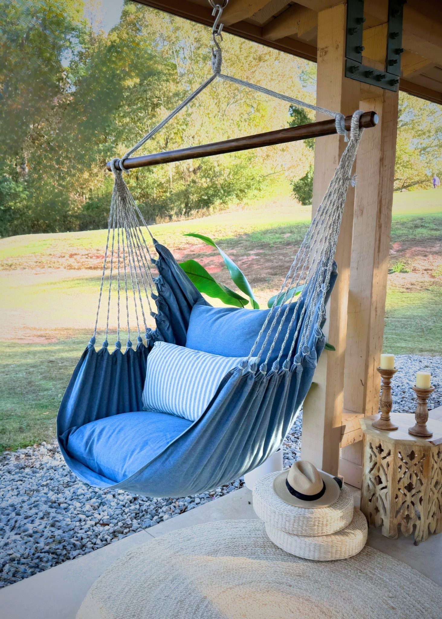 Blue hammock chair with cushions hanging from a wooden structure in an outdoor setting.