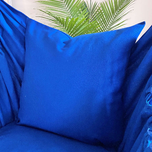 Blue pillow on a blue chair with green leaves in the background