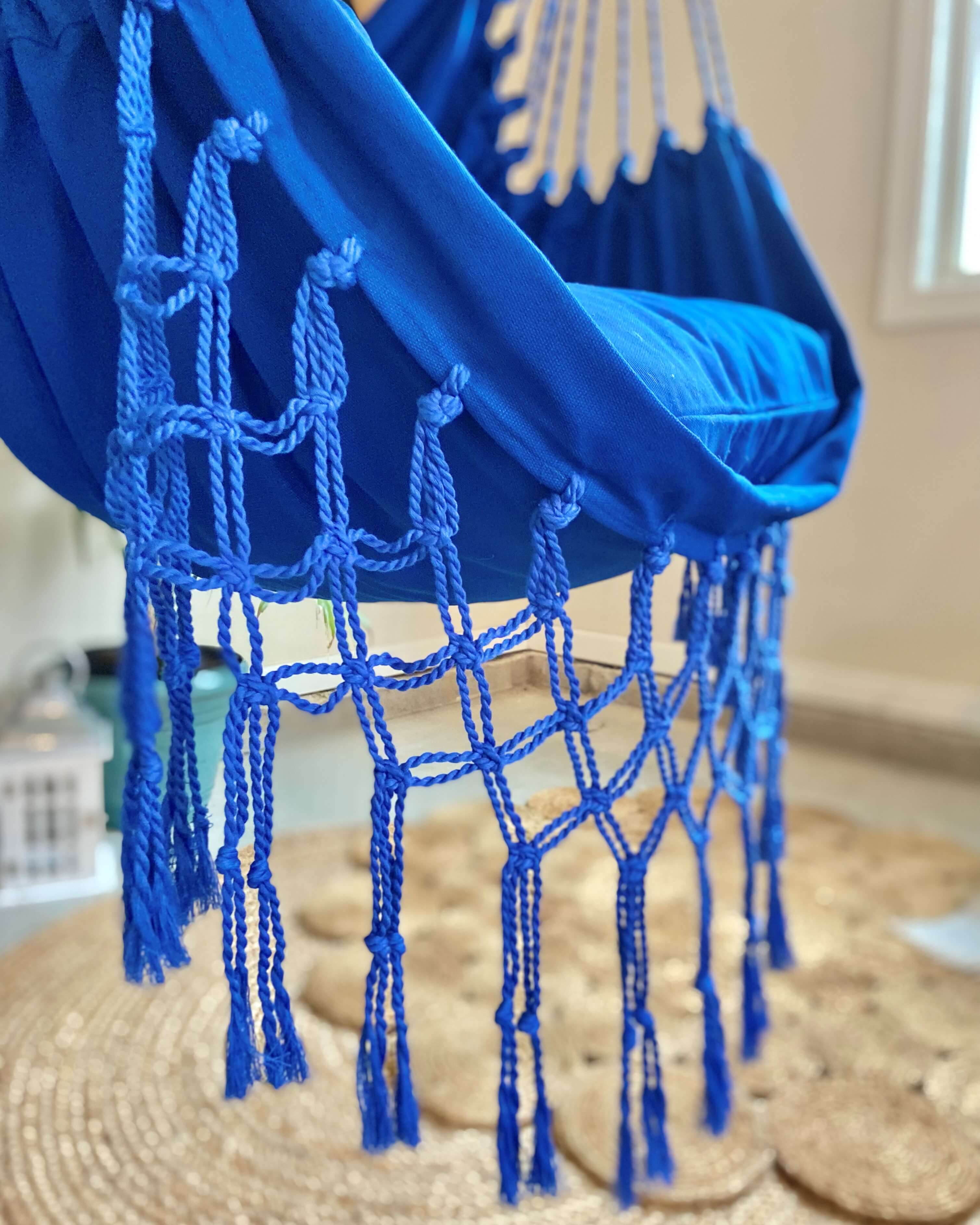 Blue hammock chair with tassels on a woven surface
