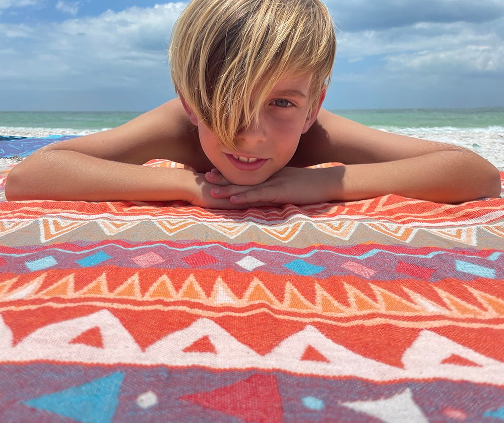 Child lying on a colorful towel at the beach with ocean and sky in the background