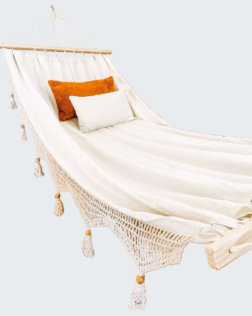 White hammock with orange and white pillows against a decorative wall.