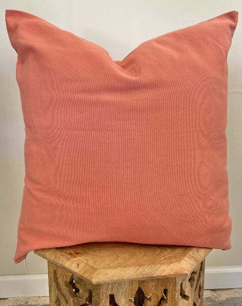 Coral pillow on a wooden stool against a neutral wall