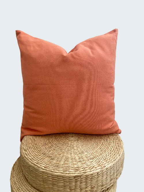 Coral pillow on a woven stool with a decorative white lattice background