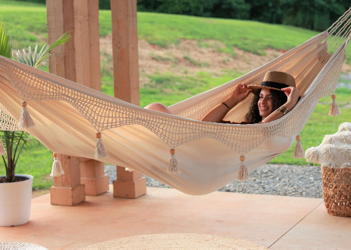 Woman relaxing in a beige hammock with tassels on a wooden deck.