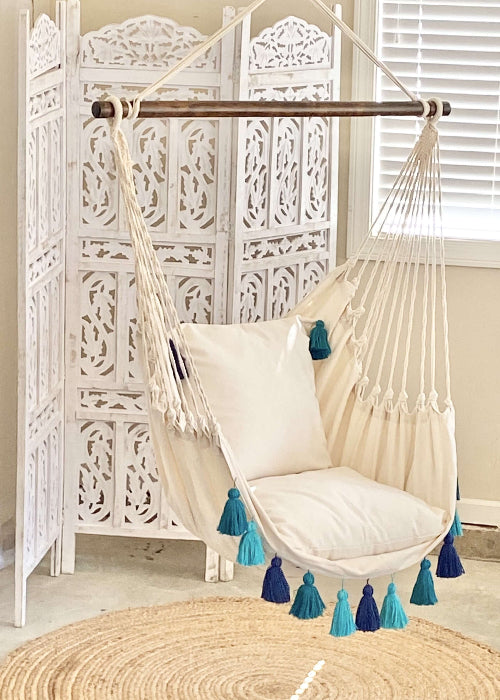 White hammock chair with blue tassels in a room with a white lattice screen and round rug.