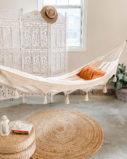 Hammock with orange pillow in a room with a round woven rug and decorative elements.