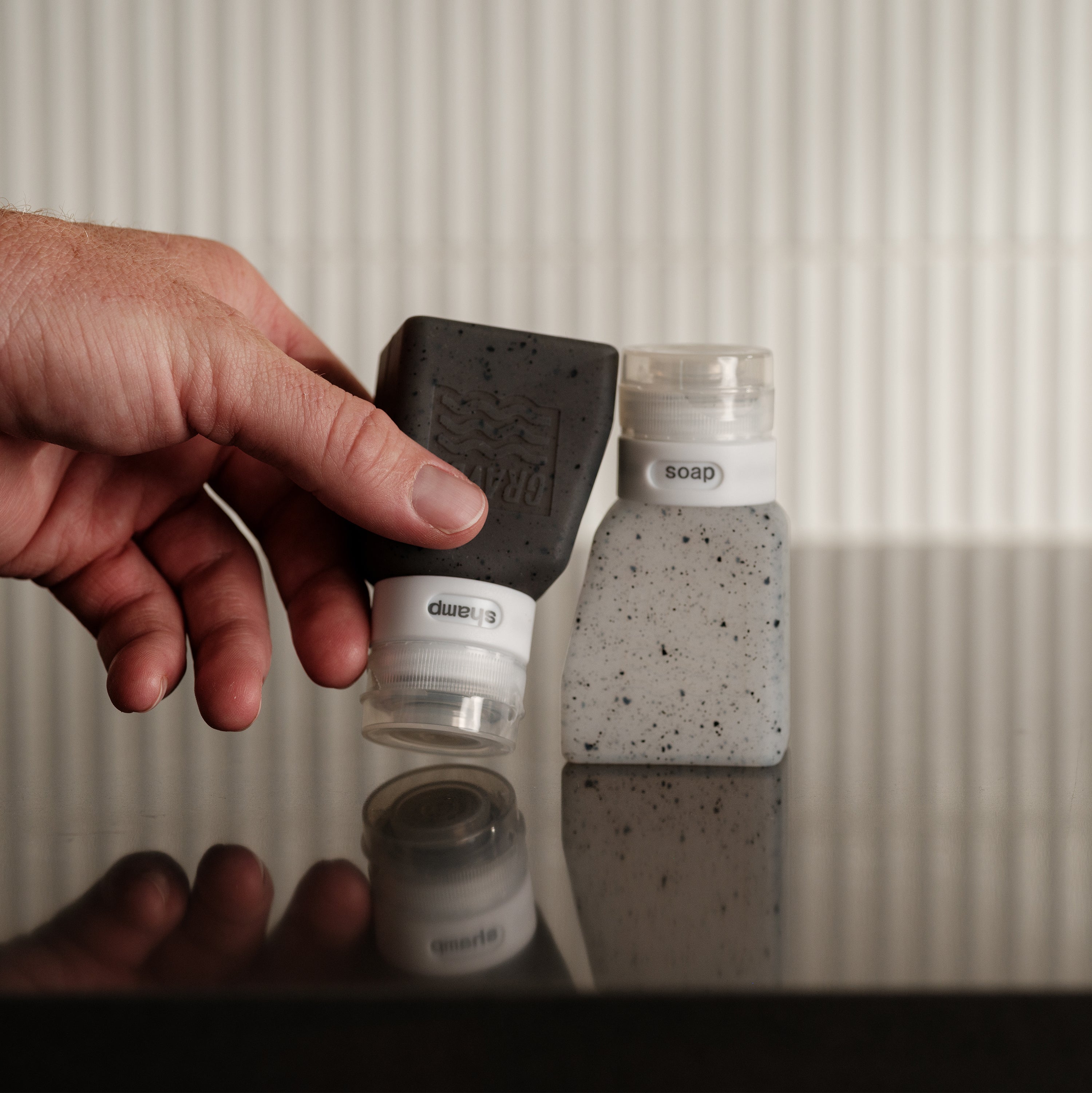 Hand holding a black and white soap dispenser with a speckled soap bar in the background.