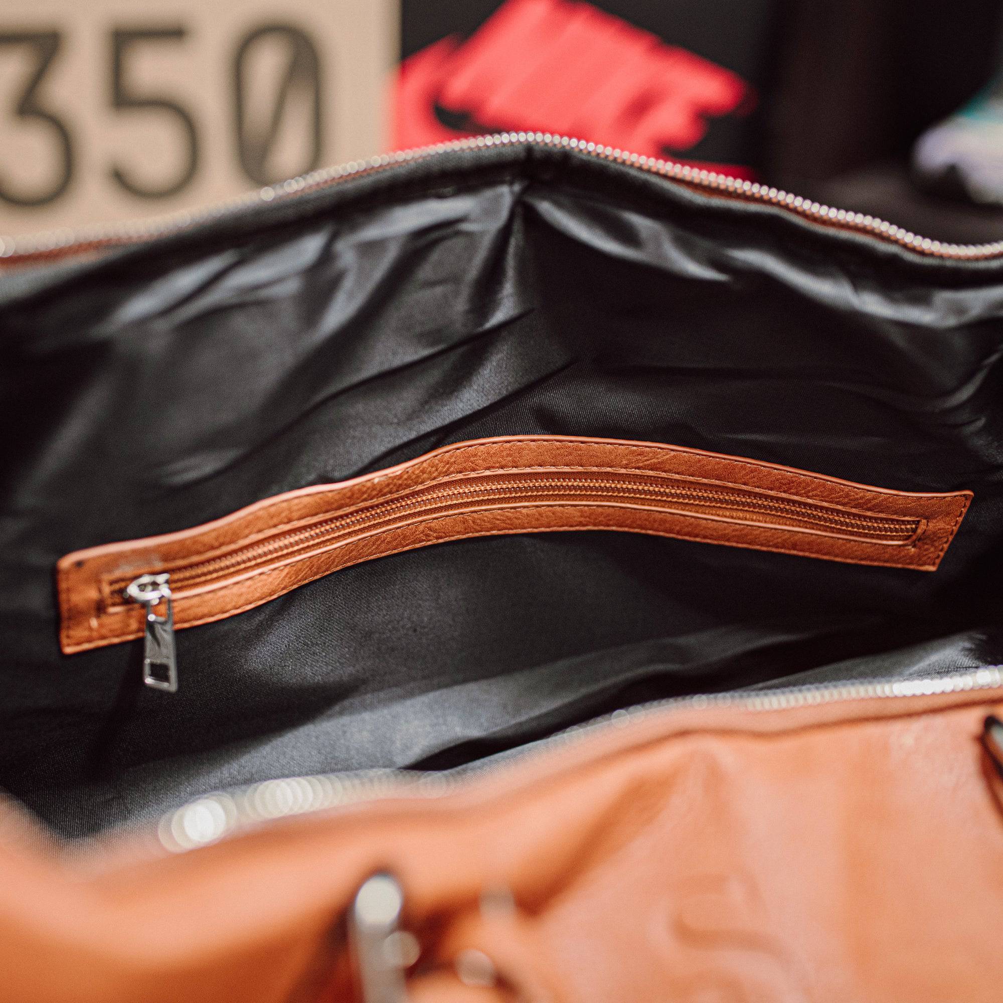 Close-up of a black leather bag with a brown zipper, blurred background