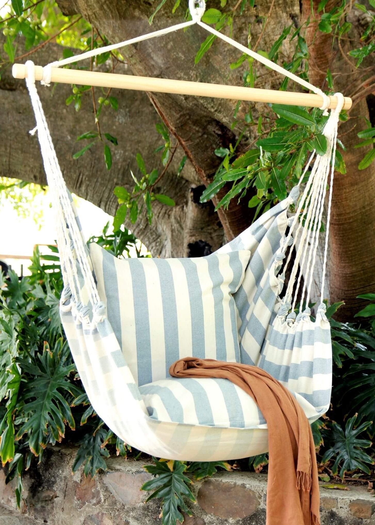 Striped hammock chair with pillow and blanket hanging from a tree