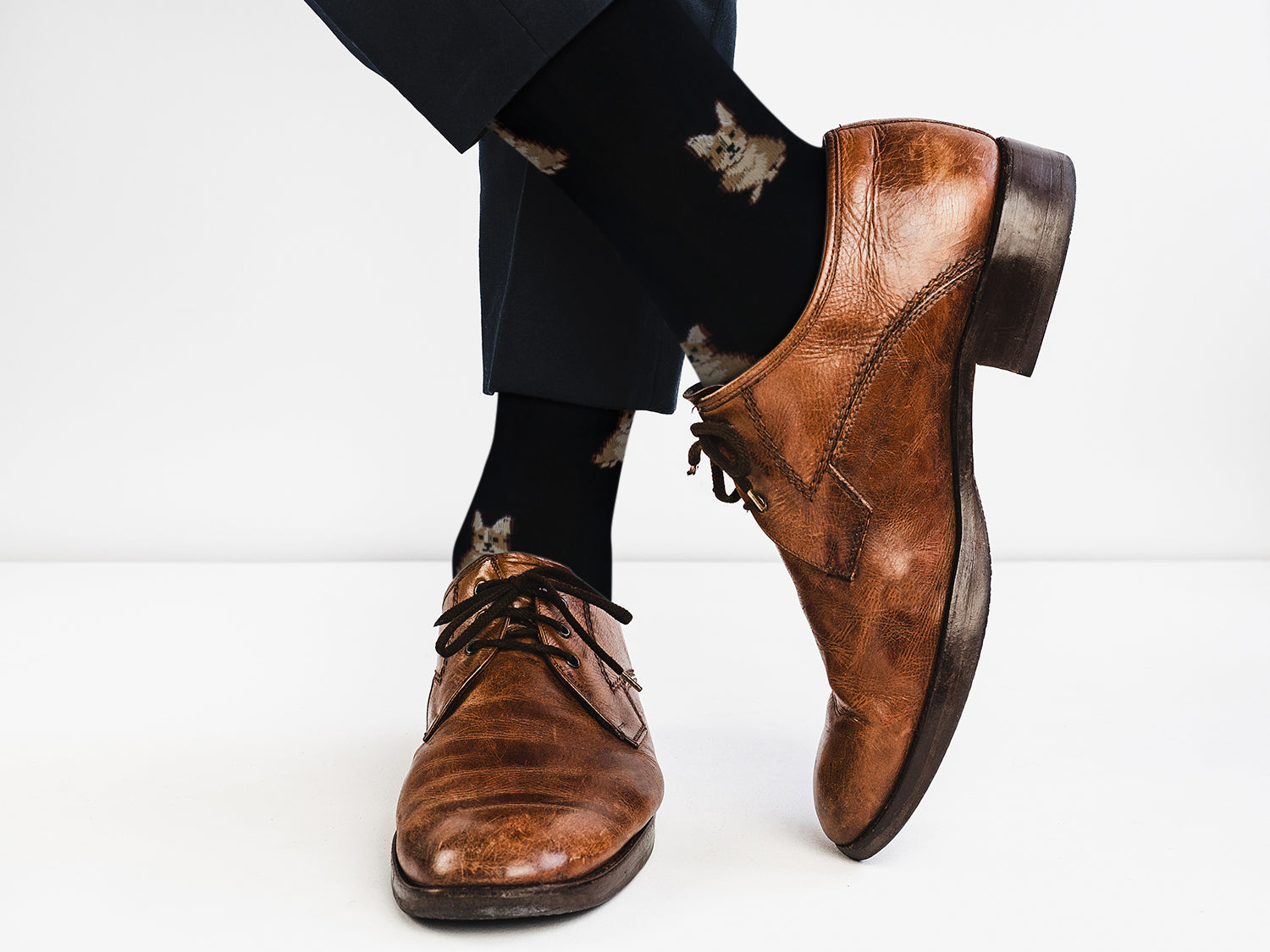 Brown leather shoes worn with black pants and patterned socks on a white background