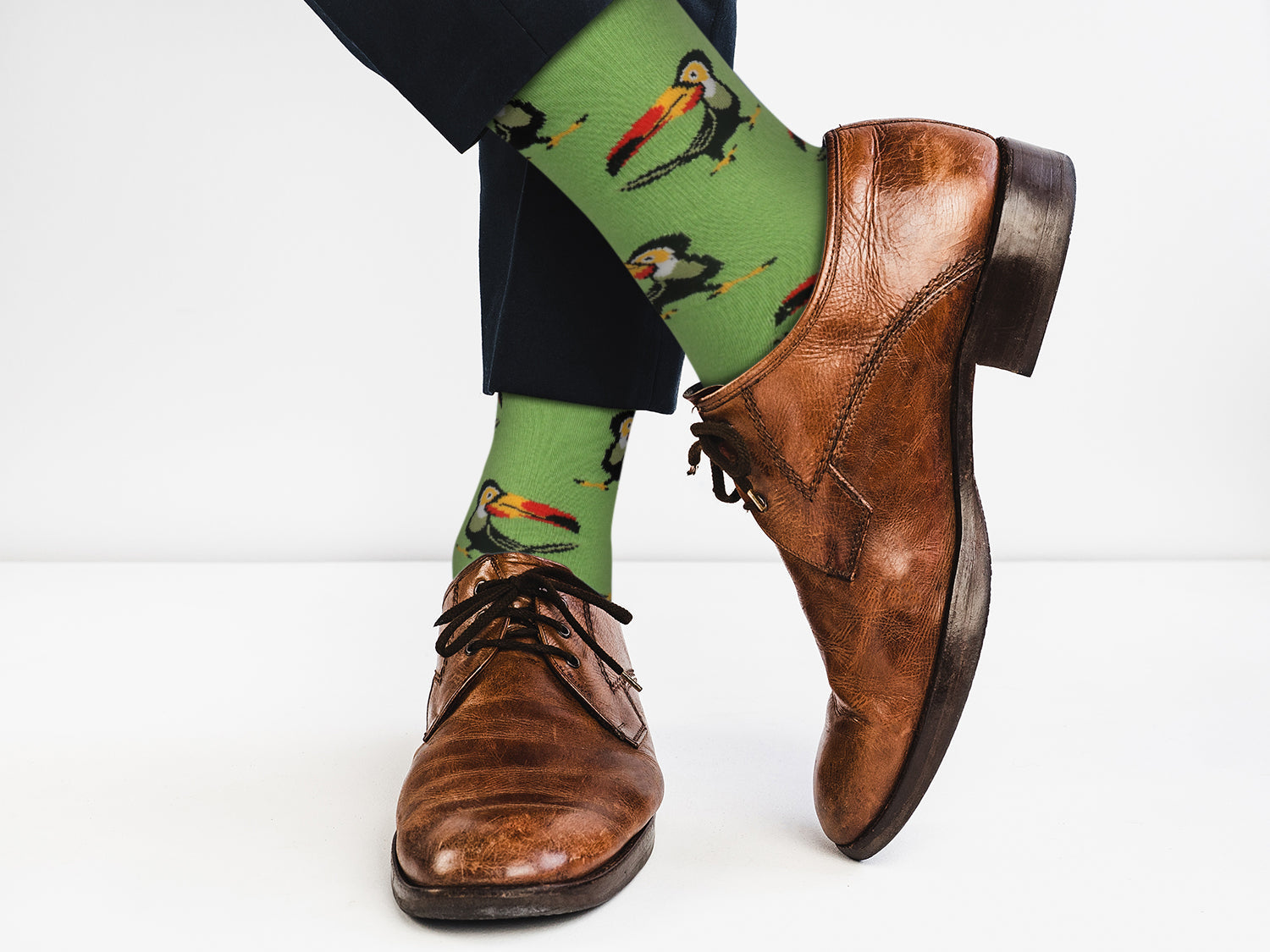 Brown dress shoes with green socks featuring toucan designs on a white background
