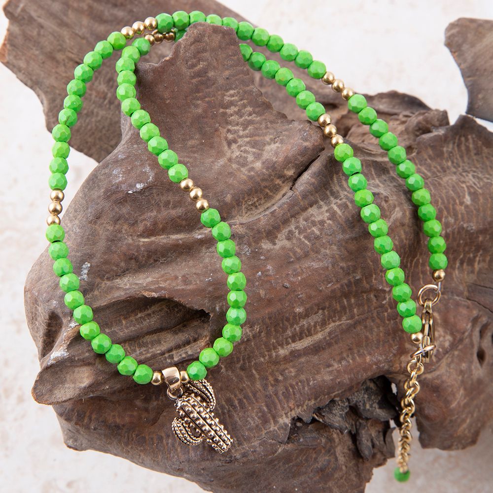 Green beaded bracelet with a gold chain and charm on a textured stone surface