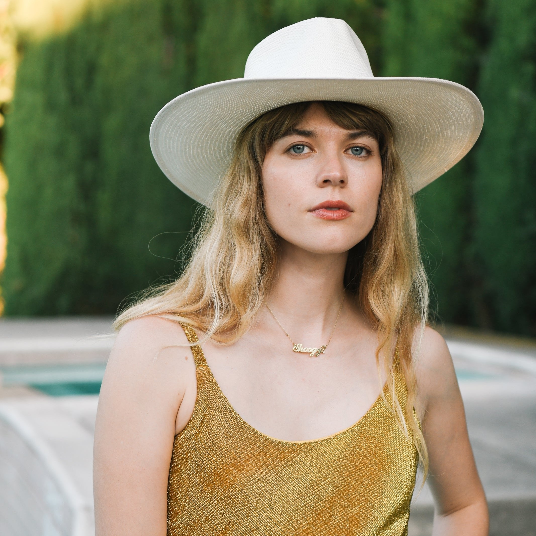 Woman wearing a white hat and gold dress with a blurred green background
