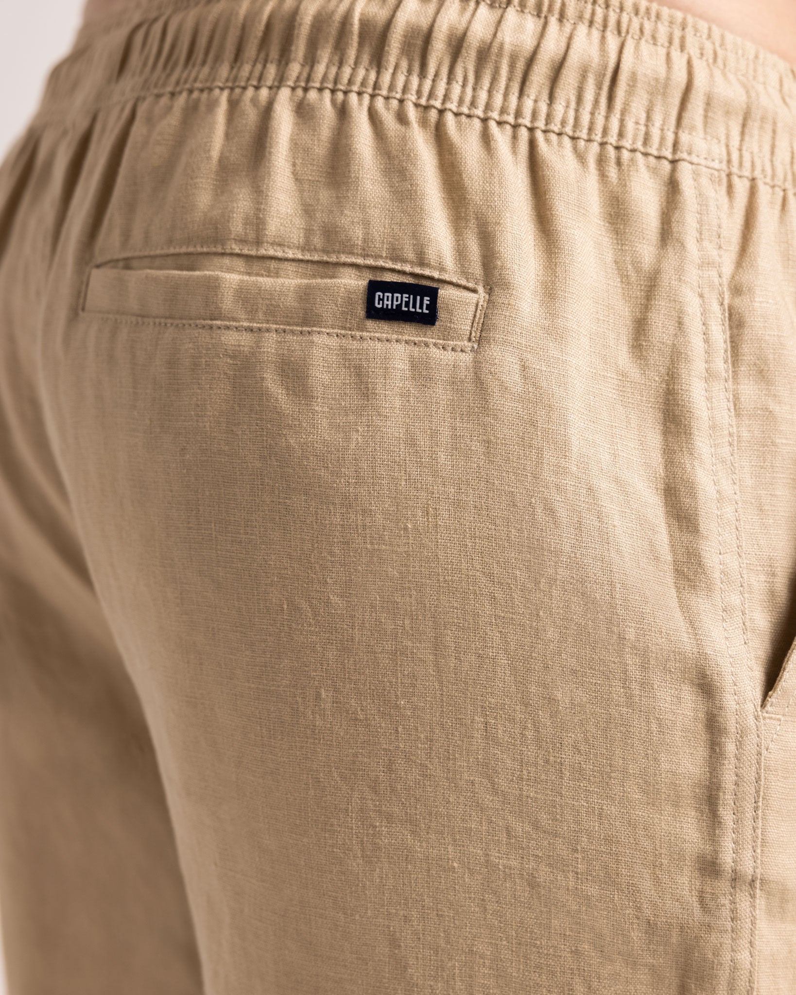 Beige pants with a brand label on the pocket against a light background