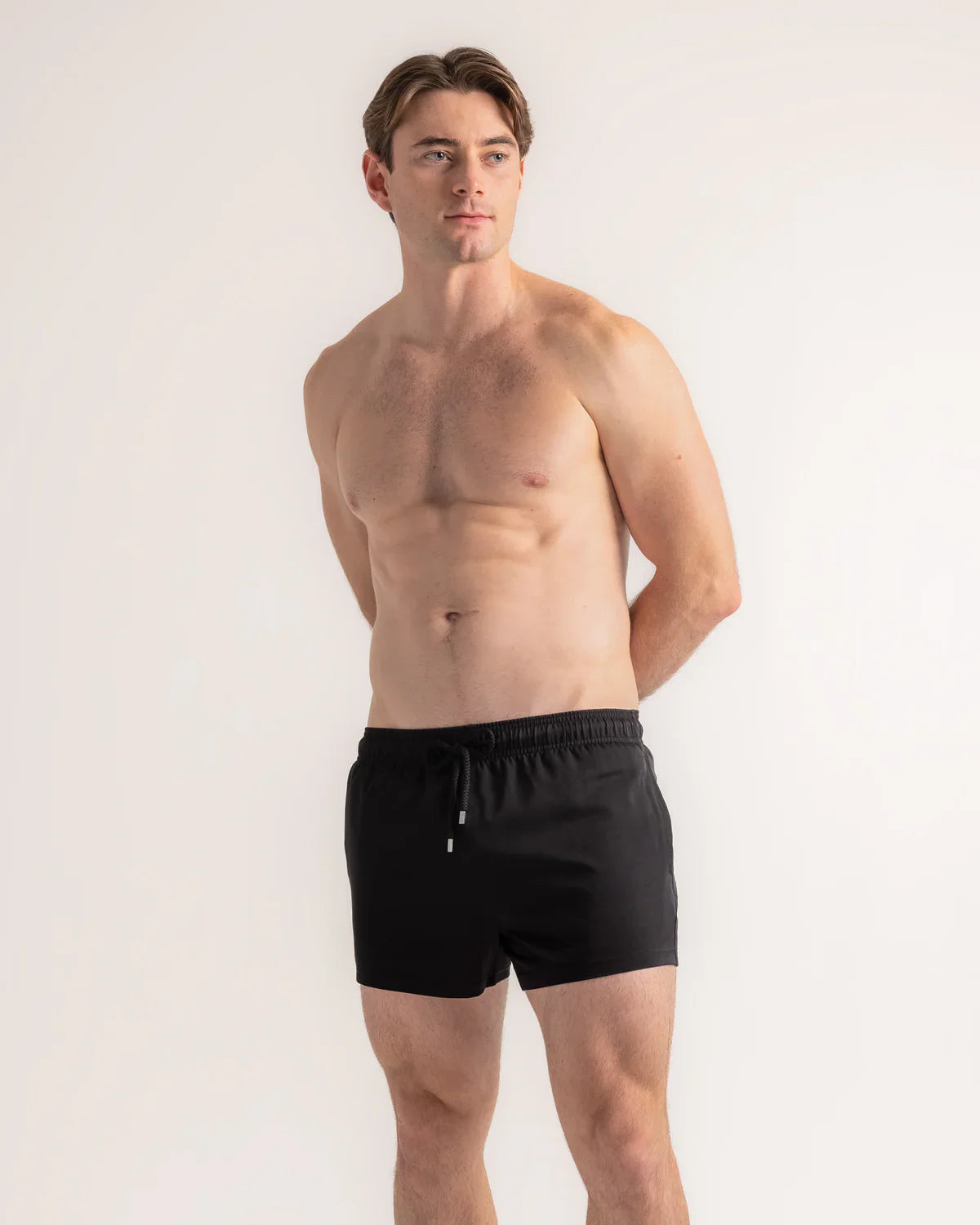 Man wearing black swim shorts against a plain background
