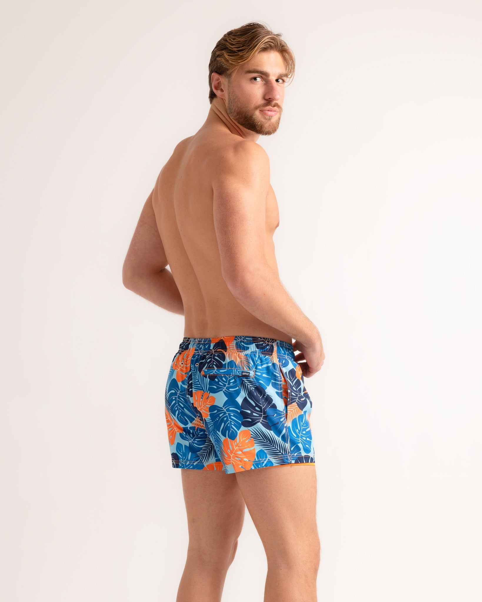 Man wearing colorful tropical leaf-patterned swim shorts on a white background