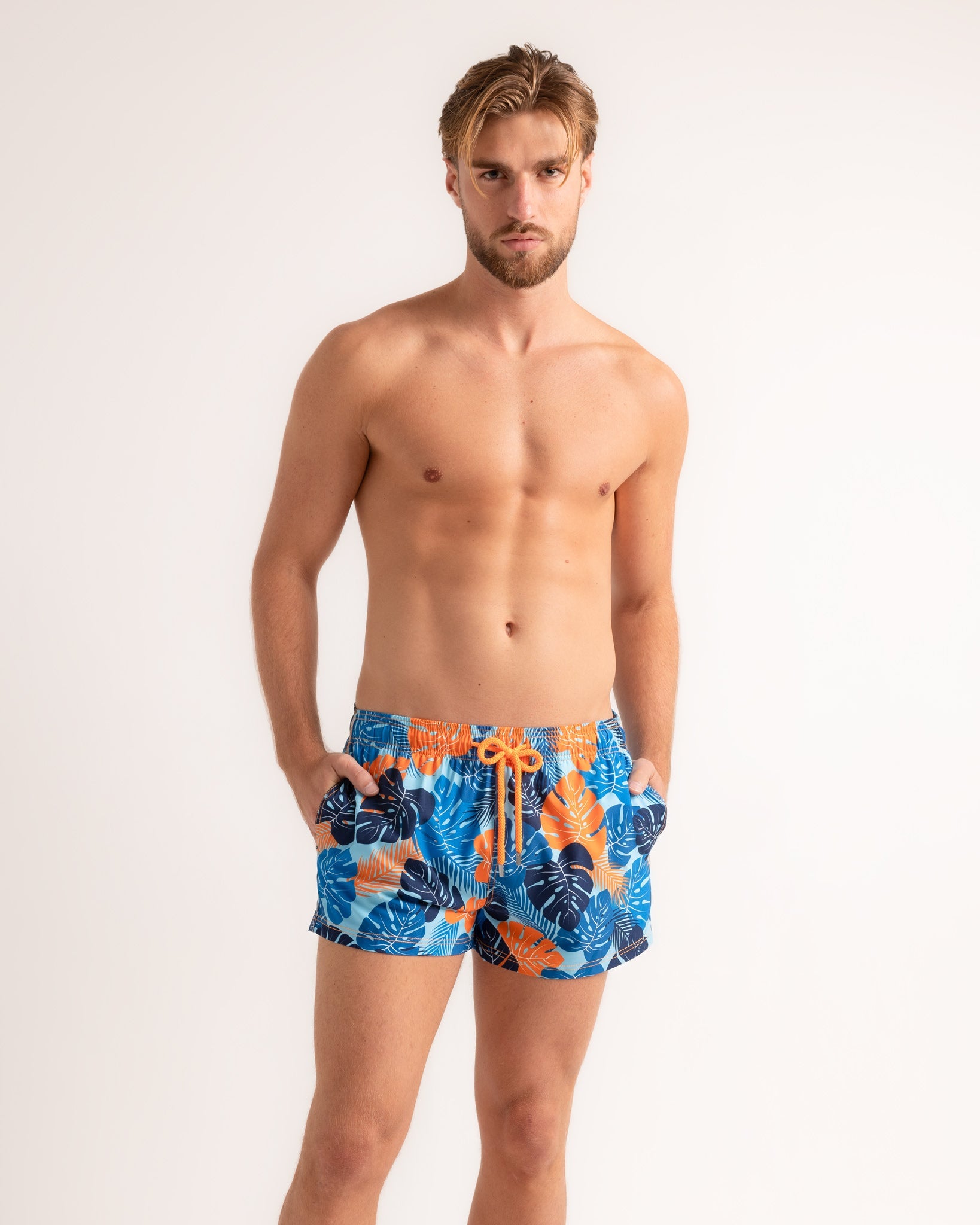Man wearing blue and orange patterned swim shorts on a plain background
