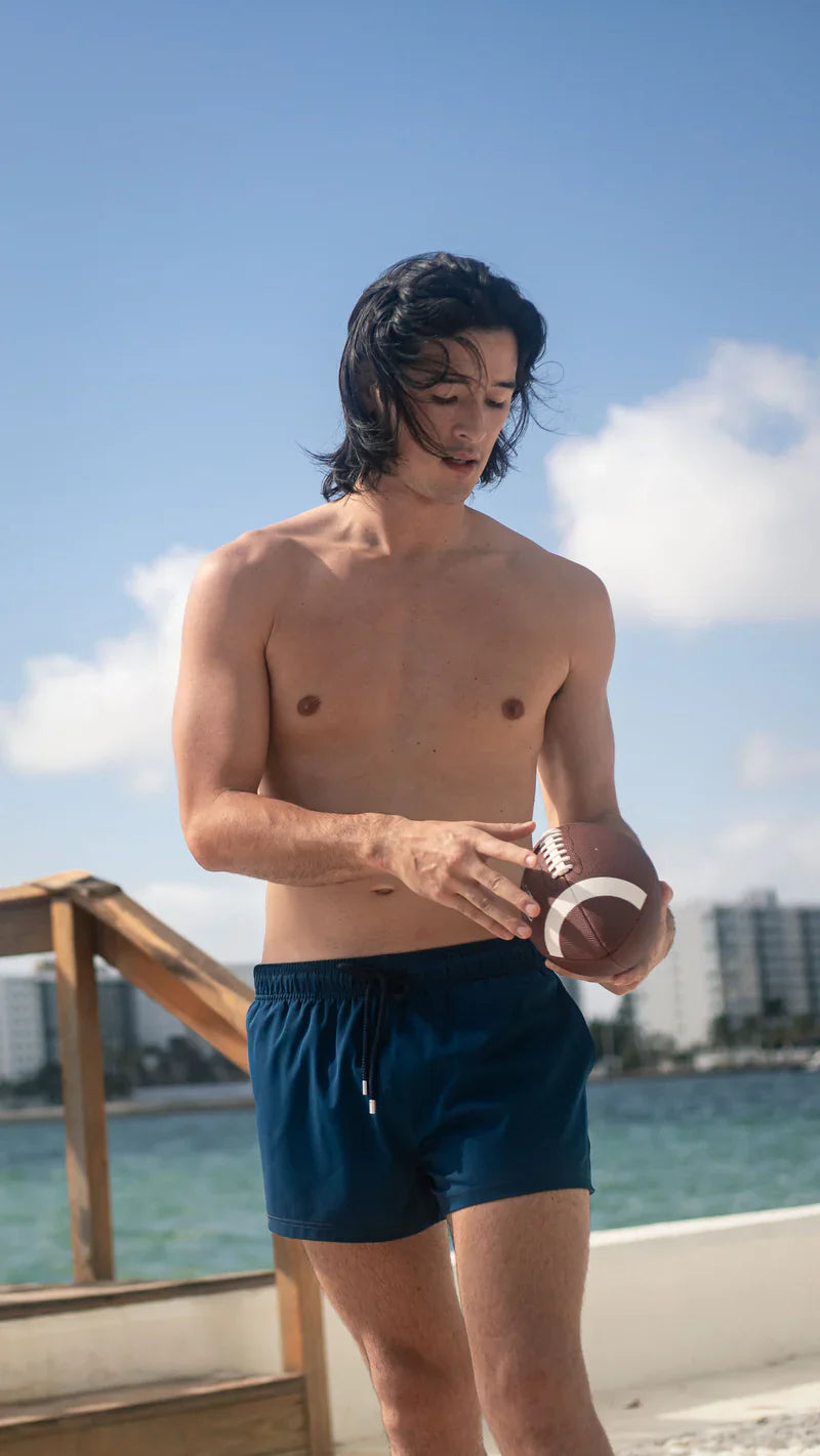 Man holding a football by the water with a clear blue sky