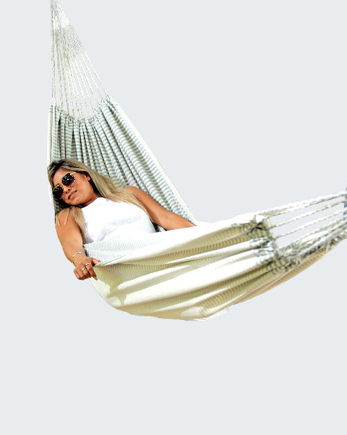 Woman relaxing in a striped hammock outdoors on a sunny day.