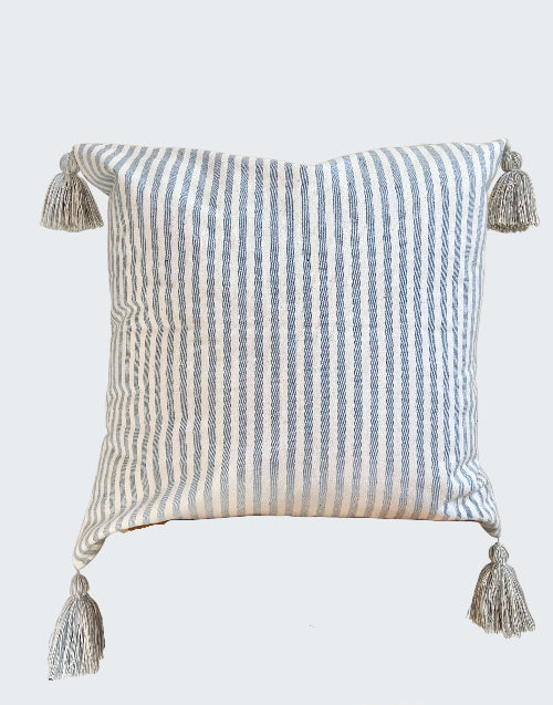 Striped pillow with tassels on a wooden stool against a beige wall
