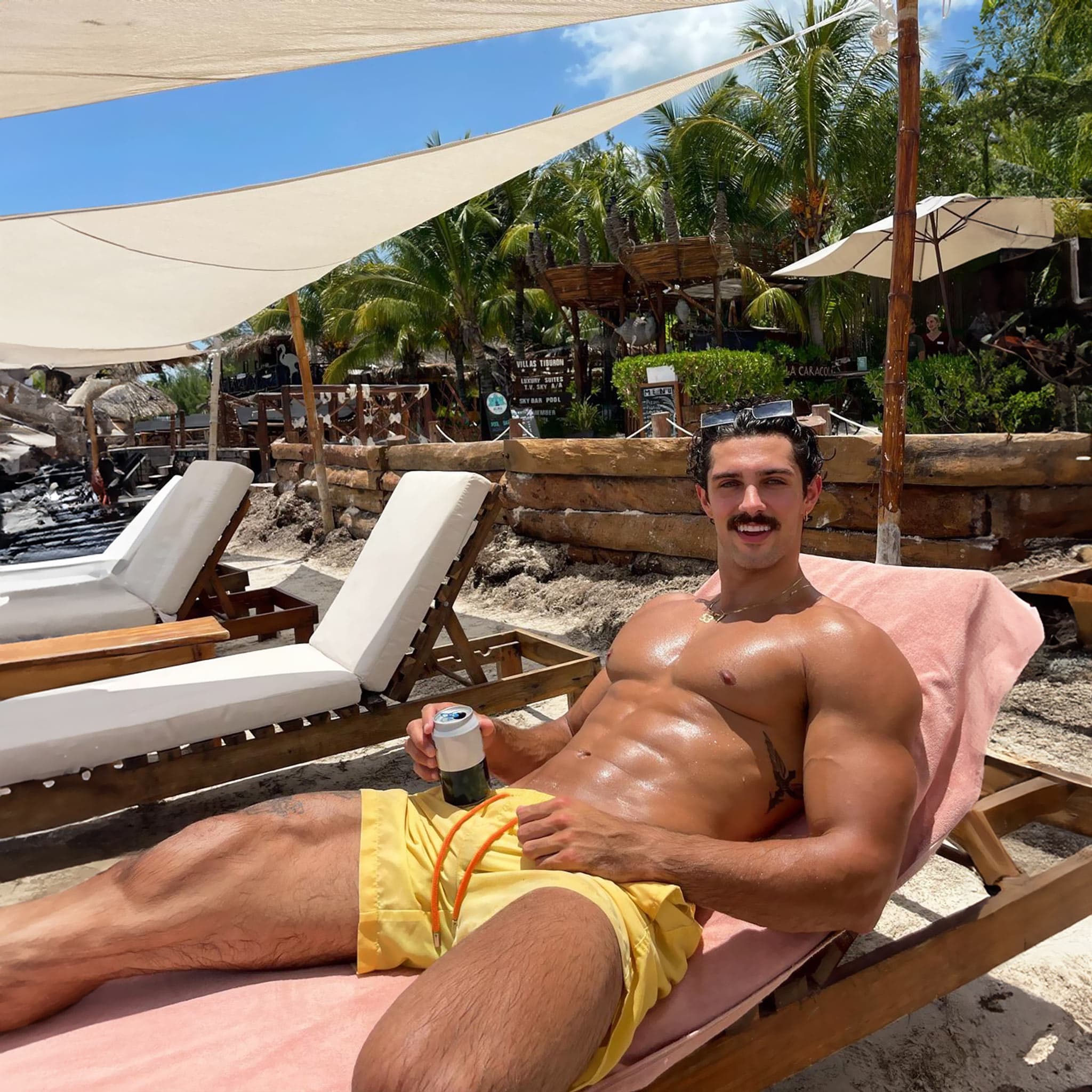 Man lounging on a beach chair with a beer, surrounded by tropical scenery.