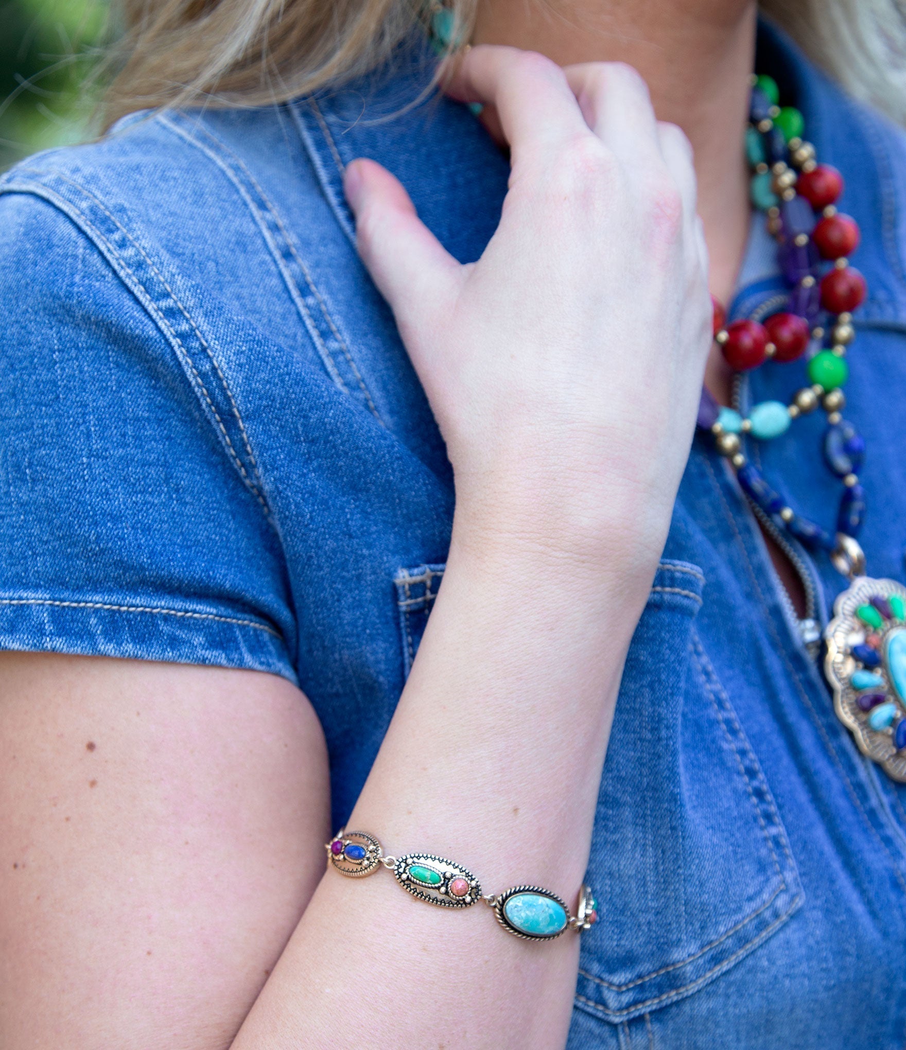 Person wearing a colorful beaded necklace and bracelet, with a blue denim shirt.