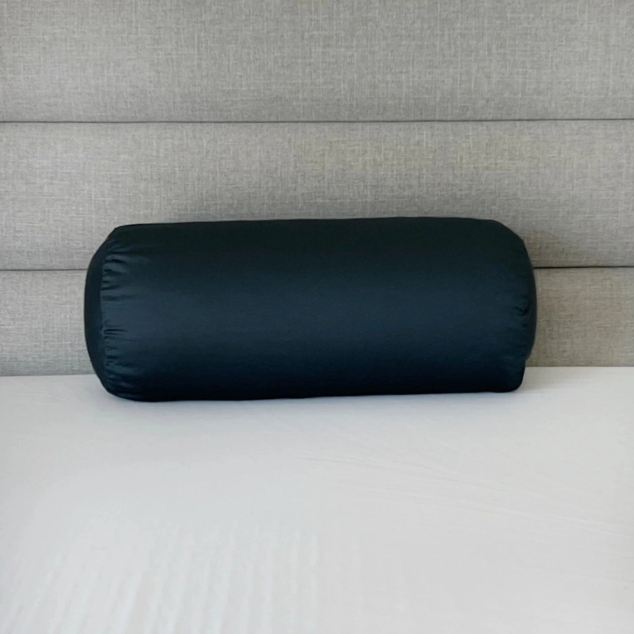 Black cylindrical pillow on a bed with a gray headboard