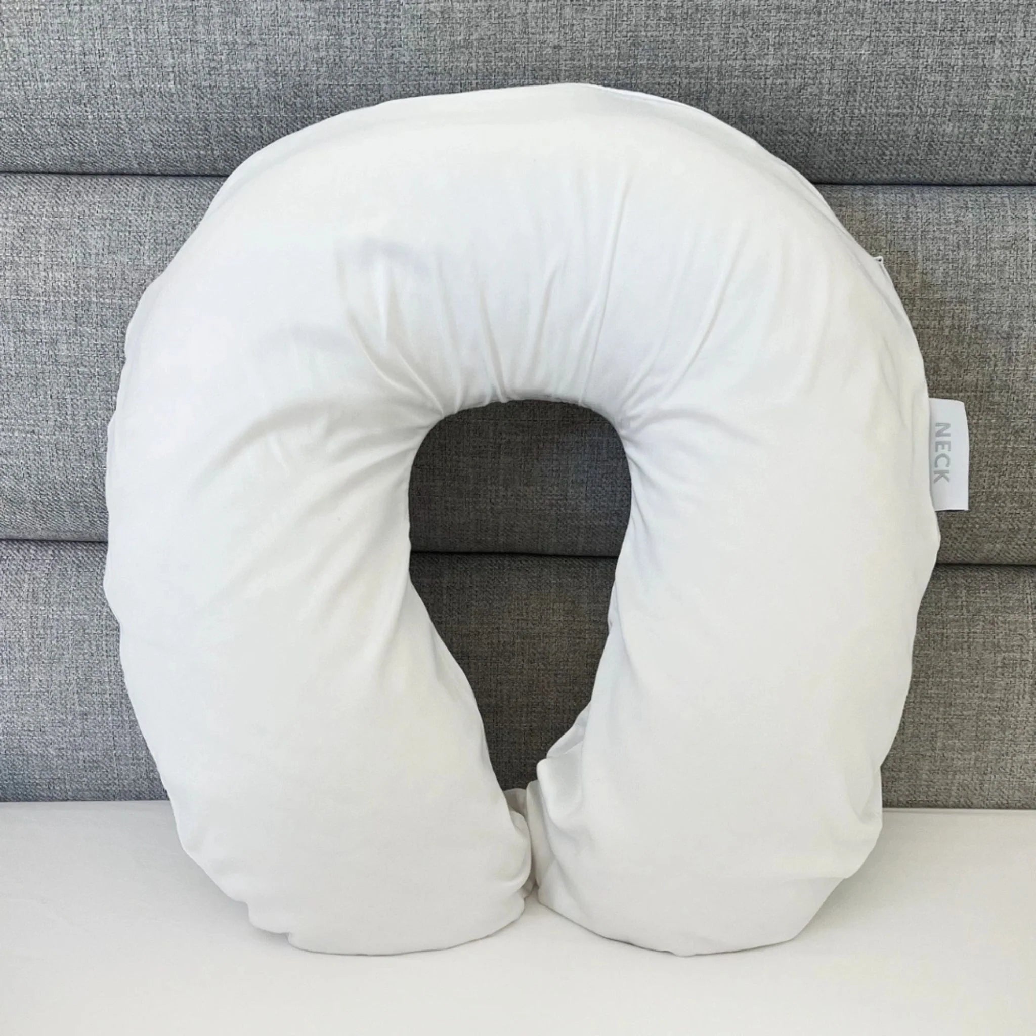 White U-shaped neck pillow on a gray couch