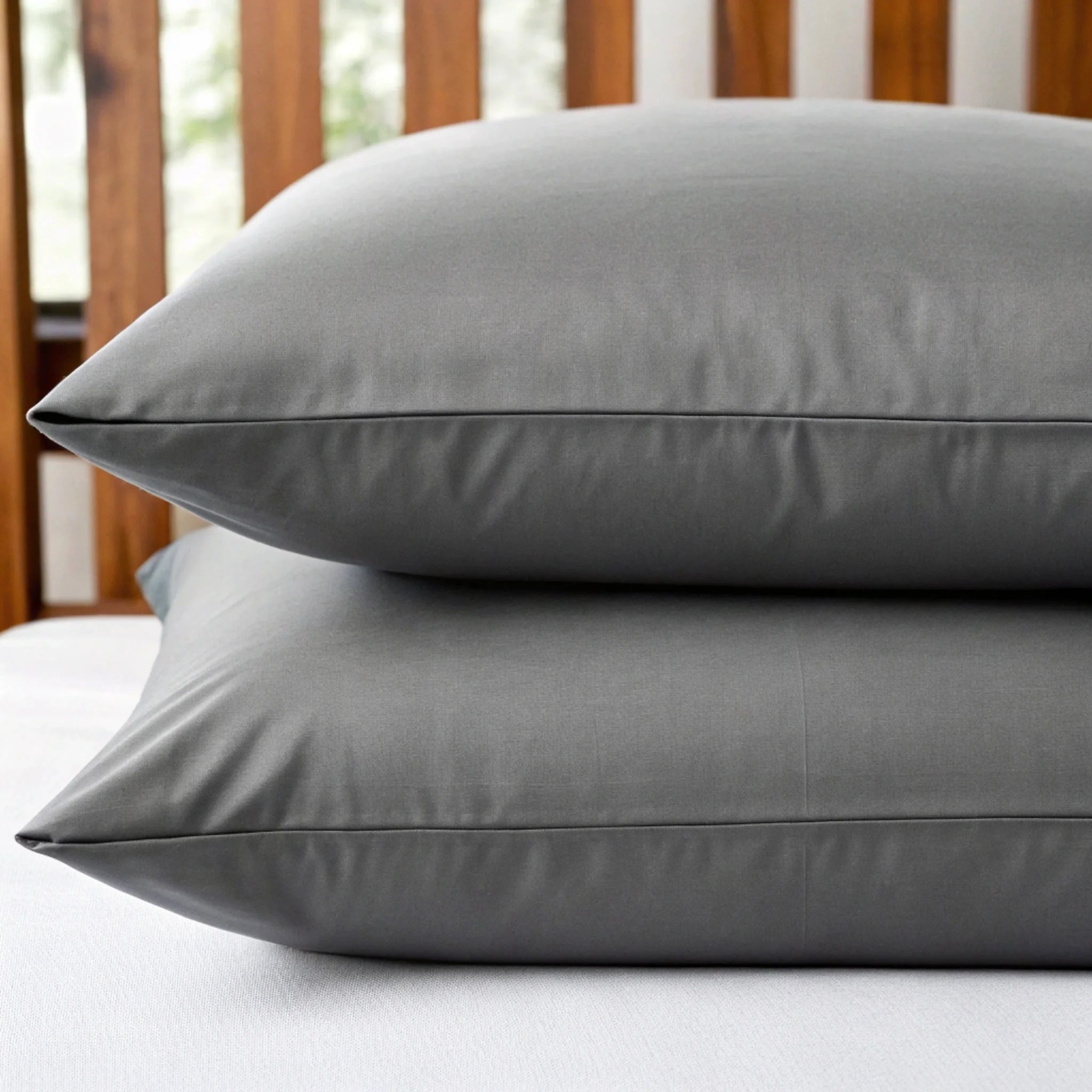 Two gray pillows stacked on a bed with a wooden headboard.