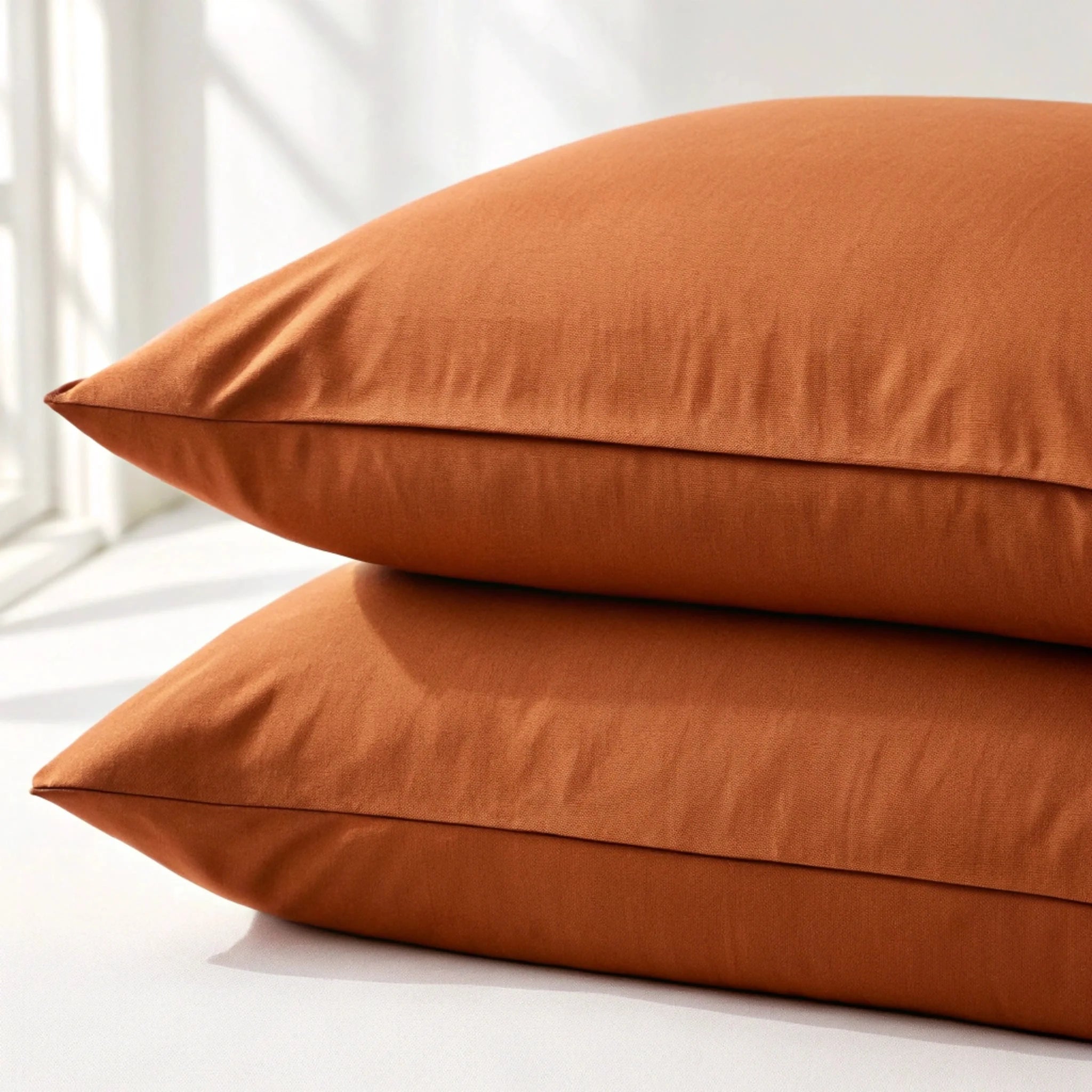 Two orange pillows stacked on a white surface with a blurred window background