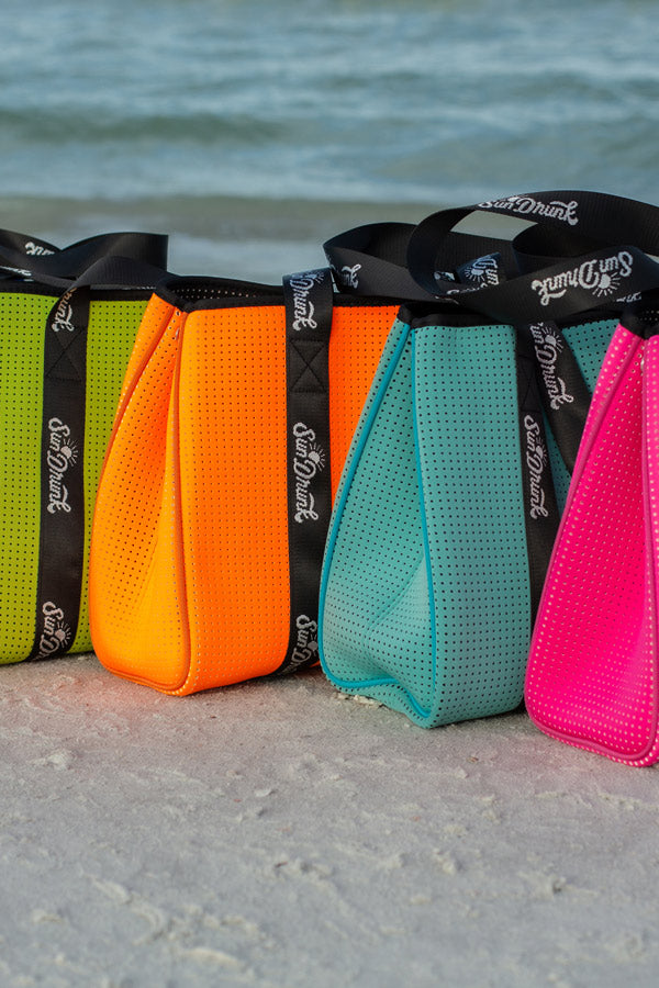 Four colorful mesh bags with black straps on a beach.