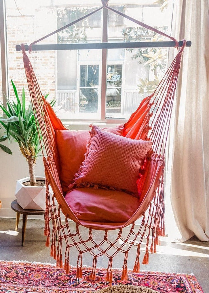 Hanging chair with pink cushions in a bright room with large windows and plants.