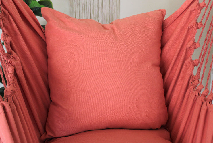 Coral-colored pillow on a hammock chair with a neutral background